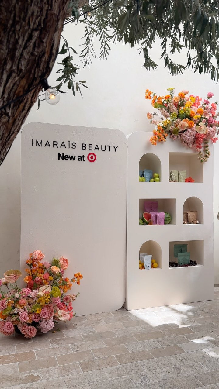 "IMARAÏS BEAUTY display at a launch event featuring 'New at Target' signage, floral arrangements, and product pouches showcased with fresh fruits in a modern, minimal shelf setup.